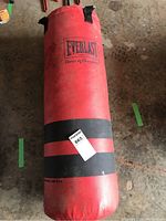 Full view of red Everlast punching bag standing upright on concrete floor with label sticker attached