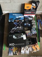 Photo showing stacked boxes of HID Xenon light conversion kits, LED headlight kits, and assorted automotive bulbs on a garage floor.