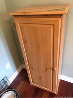 Closed view of the wooden cupboard, showing front door and knob.