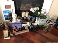 Overview of various home decor items on a hearth including candles, artificial flowers, picture frames, signs, and small decorative pieces.