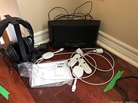 Photo showing full set including black Sony wireless stereo headphones on stand, transmitter, power adapters, cables, remotes, and user manual on hardwood floor.