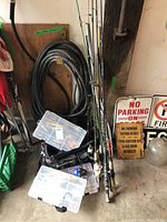 Photo showing several fishing rods standing against a wall next to storage boxes and fishing nets.