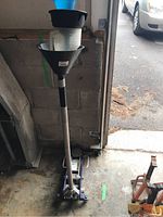 Full view of the floor jack standing upright with funnels and measuring cups stacked on the jack saddle in a garage environment.