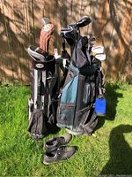 Two golf bags, one marked Mizuno and the other smaller black and grey bag with clubs, set on grass with pair of Etonic golf shoes in front.