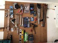 Photo of pegboard filled with various hand tools including saws, wrenches, staple gun, pliers, and standout large hand saw with leather handle
