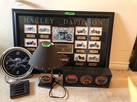 Framed collection with multiple Harley Davidson motorcycle models and years, placed on floor with lamp, clock, and light box around it