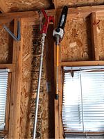 Photo of Ryobi Expand-It power saw attachment and tree pruner attachment hanging on a wooden workshop wall.