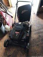Front-angle view of mower deck, wheels, engine cover, and attached grass catcher bag
