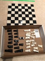 Photo showing black and white marble chess pieces arranged in a box with the chess board behind them, viewed from above.