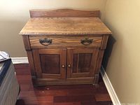 Front view of oak washstand showing drawer with metal handles and two cupboard doors with brass knobs.