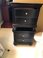 Two stacked black nightstands showing front view with two drawers each and round silver knobs.