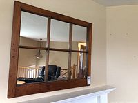 Full frontal photo of the pine wood framed window pane style mirror mounted on wall above white mantle, showing the six pane division and clear reflective glass.