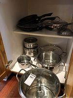 Image showing stainless steel pots with lids of various sizes arranged on bottom shelf.