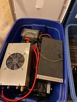 Blue plastic bin holding multiple electronic components including Jensen inverter, DC power supply, speaker and radio head