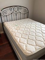 Full view of the queen size metal bed with decorative headboard and mattress on hardwood floor.