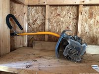 Side view of Ryobi Expand-It tiller attachment showing blades, handle, and dirt residue.