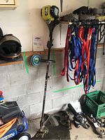 Full length view of Ryobi weed trimmer standing against a cinder block wall with hanging items nearby