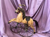 Side view of wooden toy horse showing painted body, metal spoke wheels, black leather saddle and horse hair mane and tail.