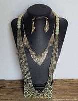 Photo of multi-strand necklace with pale green and silver-tone beads, triangular pendant and matching earrings on display stand.