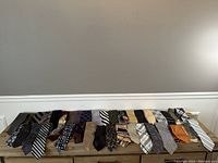 Photo showing 19 assorted men's neckties laid out in a row on a wooden surface.