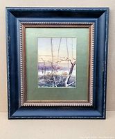Framed watercolour artwork showing the full frame, green matte border, and painting of trees by water.
