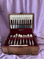Closed wooden box with velvet lining holding 12 knives in top compartment and forks and spoons in lower compartment.