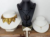 Front view of chin-level necklace display showing three necklaces - gold leaf motif choker, black beaded heart pendant necklace, and pearl bead necklace alongside the displayed clip-on earrings.