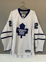 Front view of white Toronto Maple Leafs hockey jersey with blue logo and sleeve stripes.