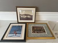 Three framed wall art pieces showing a harbor photograph and two colored prints including ice skaters and a winter street scene.
