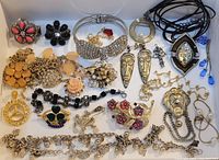 Full layout photo showing a large assortment of costume jewellery including pendants, earrings, necklaces, bracelets, and brooches in various styles and colors.