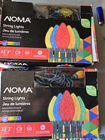 Two boxes of NOMA string LED lights showing packaging with colorful C9 bulb illustrations, 33'3" length and 50 bulbs