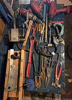 Wide view of assorted tools laid on a blue surface including drills, pliers, and odd shaped tools.