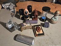 Photo of the full assortment on surface showing all items including candle holder, Buddha figurine, sandtimer, carved egg, carved figurine, metal case, and various boxes.