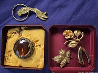 Set of five vintage brooches displayed in jewelry boxes, showing various designs and metal colors.