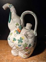 Side view of the ceramic elephant teapot showing colorful floral and butterfly motifs and green accents on tusks and trunk.