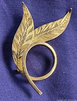 Front angled view of sterling silver brooch showing detailed engraved leaf design and curled stem loop