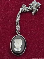 Full view of black and frosted glass cameo necklace laid on red fabric background.