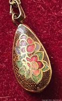Close-up of teardrop-shaped cloisonné pendant with multi-colored floral design on textured gold-tone background.