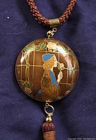 Front and close-up views of cloisonne pendant showing woman holding rose and attached to brown braided cord necklace