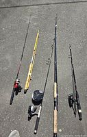 Overview photo showing four fishing rods with attached reels laying on ground