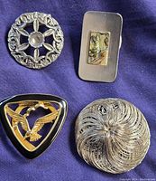 Four scarf pins laid on dark purple fabric showing various designs and metal tones