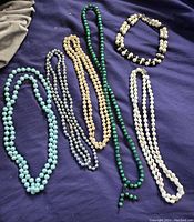 Full view of six pearl style necklaces in various colors on dark fabric background