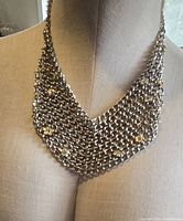 Front view of the silver tone draping necklace displayed on a mannequin, showing the chainmail design and flower accents