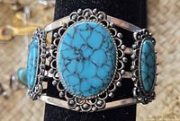 Close-up image showing the central and side turquoise cabochons in decorative silver settings on a thick band bracelet.