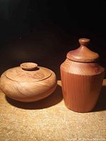 Photo showing both wood turned containers side by side on wooden surface against dark background.
