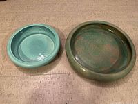 Two round pottery planters side by side with different glaze colors, one turquoise blue, one mottled green/brown