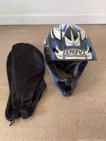 Front angle view of AGV RC-5 Junior full-face motorcycle helmet with blue, white and black color scheme, displayed on floor alongside black helmet bag.