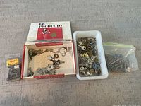 Multiple small keys of various designs inside a white container and a vintage 'El Producto' cigar box used to hold some keys.