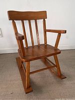 Side angled view of wooden children's rocking chair showing slatted backrest, armrests, seat panels, and rocker base.