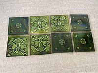 Photo showing eight 6x6 green ceramic tiles arranged in two rows of four, alternating floral and geometric embossed designs.